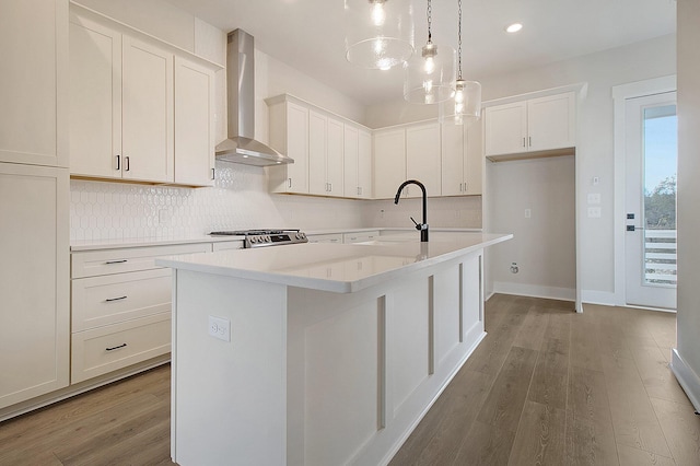 kitchen featuring wall chimney exhaust hood, a sink, light wood-type flooring, an island with sink, and backsplash