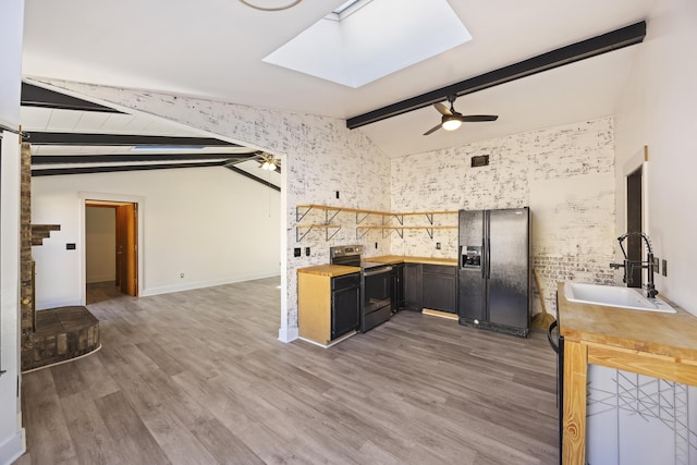 kitchen featuring sink, vaulted ceiling with skylight, black fridge, and electric stove