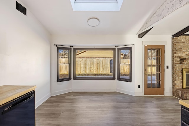 unfurnished dining area with a fireplace, dark wood-type flooring, and vaulted ceiling with skylight