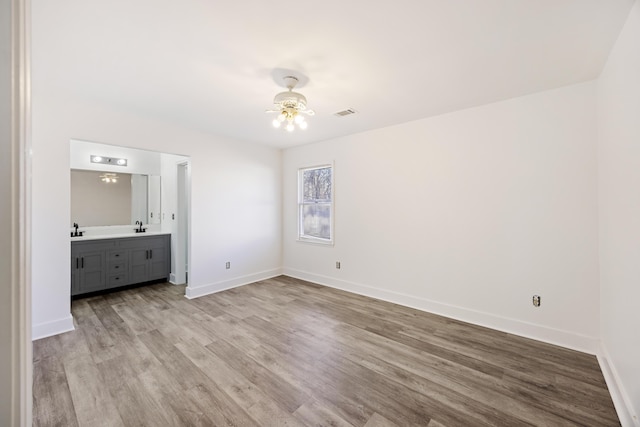 unfurnished bedroom featuring ceiling fan, sink, connected bathroom, and light wood-type flooring