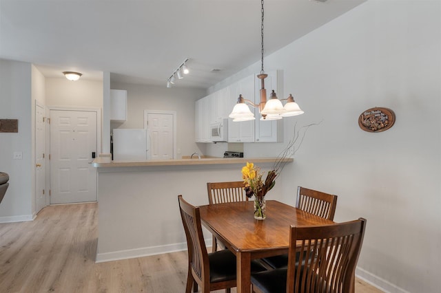 dining room with an inviting chandelier, sink, light wood-type flooring, and rail lighting