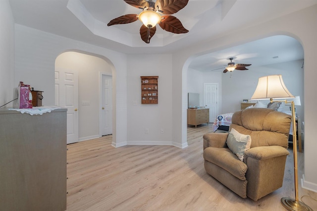 living area with a tray ceiling, light hardwood / wood-style floors, and ceiling fan