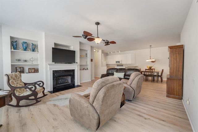 living room featuring built in features, a high end fireplace, light wood-type flooring, and ceiling fan