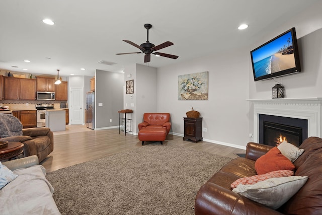 living room with baseboards, ceiling fan, recessed lighting, light wood-style flooring, and a glass covered fireplace