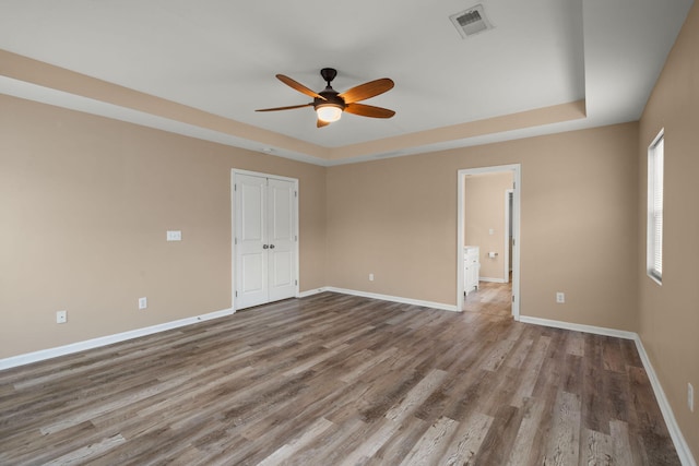 spare room with a raised ceiling, wood finished floors, visible vents, and baseboards