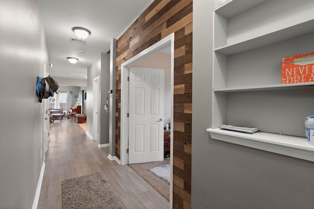 hall with visible vents, baseboards, light wood-style floors, and wooden walls