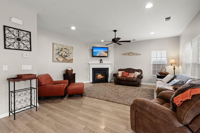 living area with a glass covered fireplace, visible vents, light wood-style flooring, and recessed lighting