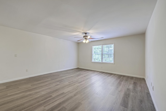 empty room with ceiling fan, wood finished floors, and baseboards