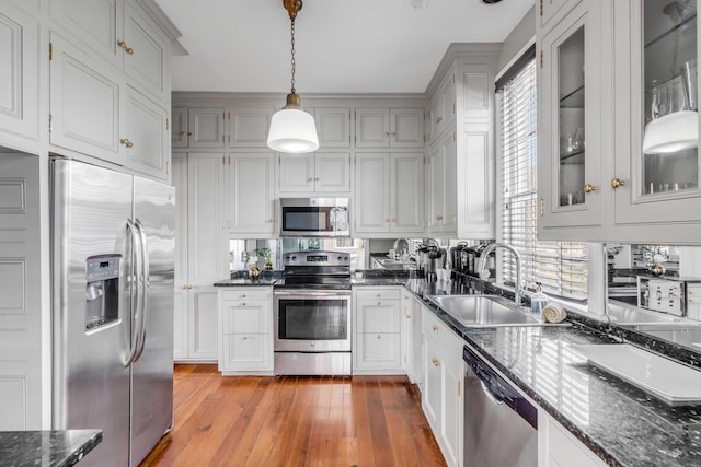 kitchen with appliances with stainless steel finishes, dark stone counters, sink, pendant lighting, and light hardwood / wood-style floors