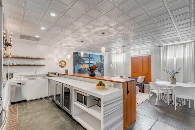 kitchen with kitchen peninsula, stainless steel appliances, sink, decorative light fixtures, and white cabinets