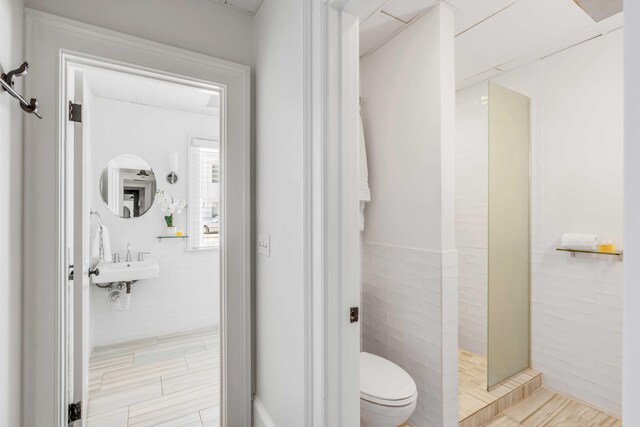 bathroom featuring sink, a shower, toilet, and tile walls