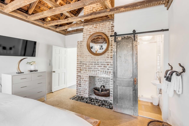 carpeted bedroom with beam ceiling, a barn door, and a brick fireplace