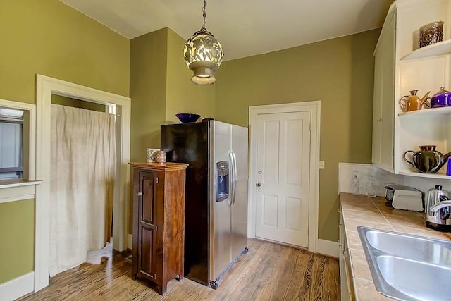 kitchen with open shelves, stainless steel fridge with ice dispenser, a sink, tile counters, and light wood-style floors
