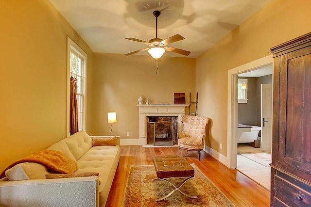 living room featuring baseboards, a ceiling fan, light wood-style flooring, and a fireplace