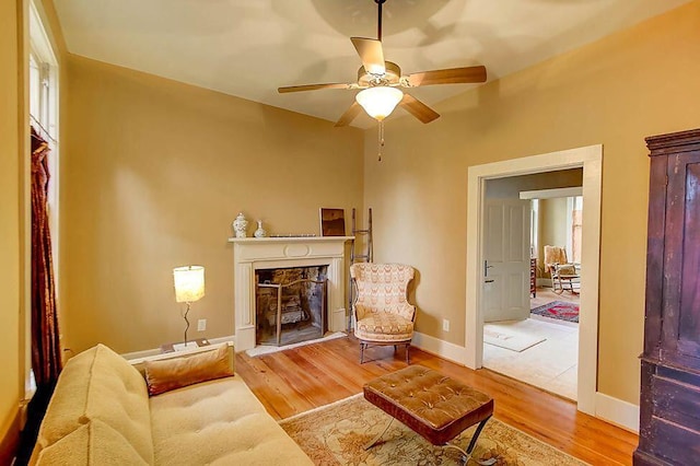 living area featuring a high end fireplace, ceiling fan, baseboards, and wood finished floors
