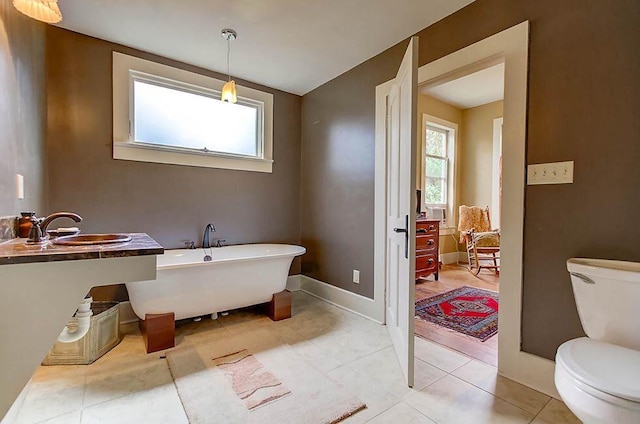 bathroom featuring baseboards, a freestanding bath, toilet, tile patterned floors, and a sink