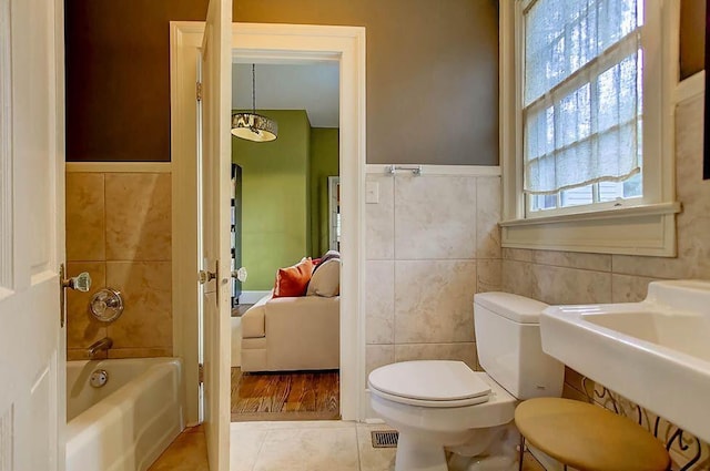 bathroom with tile walls, toilet, a healthy amount of sunlight, and a tub to relax in