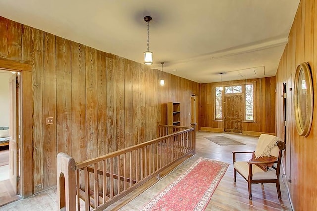 hallway with wood finished floors, an upstairs landing, baseboards, and wood walls