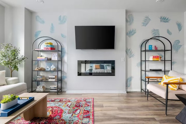 living room featuring wood finished floors, a glass covered fireplace, and baseboards