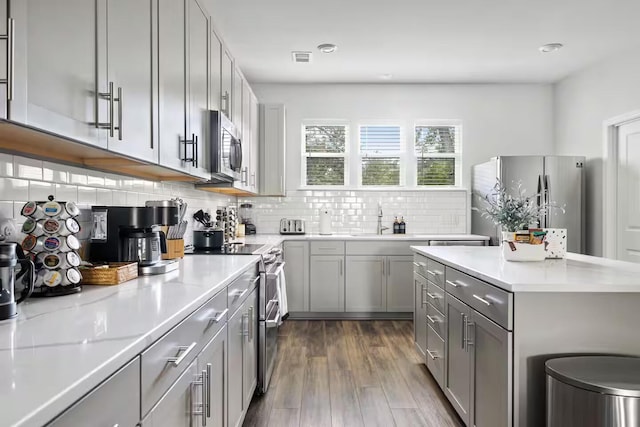 kitchen with appliances with stainless steel finishes, gray cabinetry, a sink, light countertops, and decorative backsplash