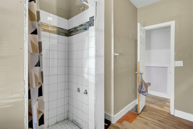 full bathroom with a tile shower, baseboards, and wood finished floors