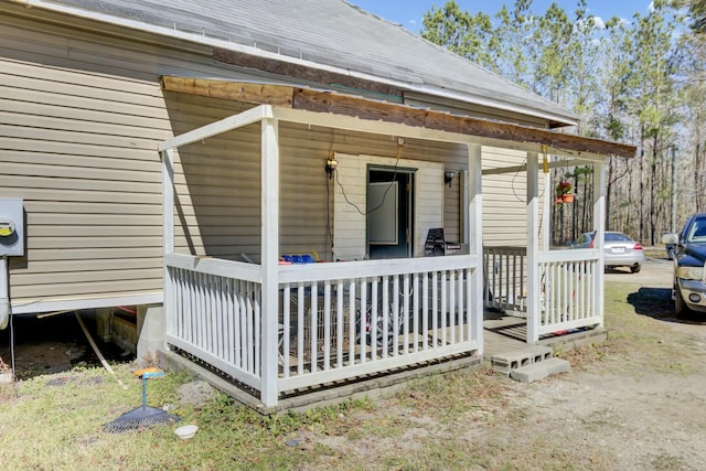 property entrance featuring covered porch and a shingled roof