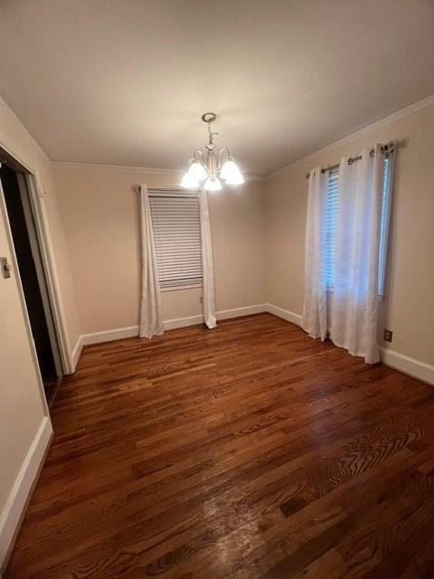 empty room featuring crown molding, a chandelier, and dark hardwood / wood-style flooring