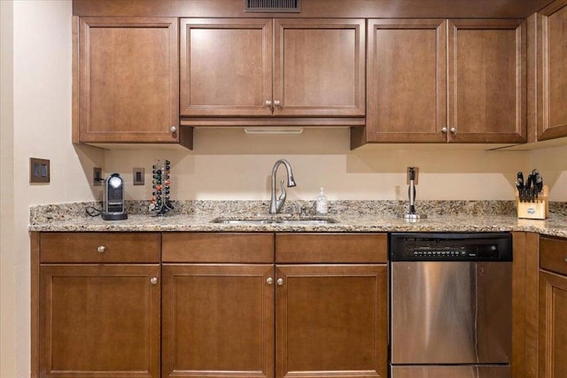 kitchen with stainless steel dishwasher, brown cabinetry, a sink, and light stone countertops