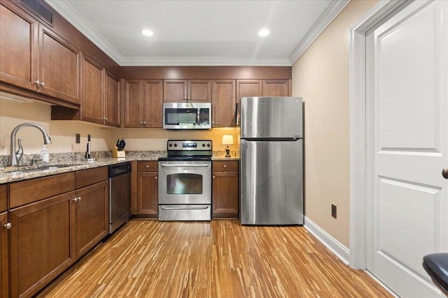 kitchen with light stone counters, crown molding, light wood finished floors, appliances with stainless steel finishes, and a sink