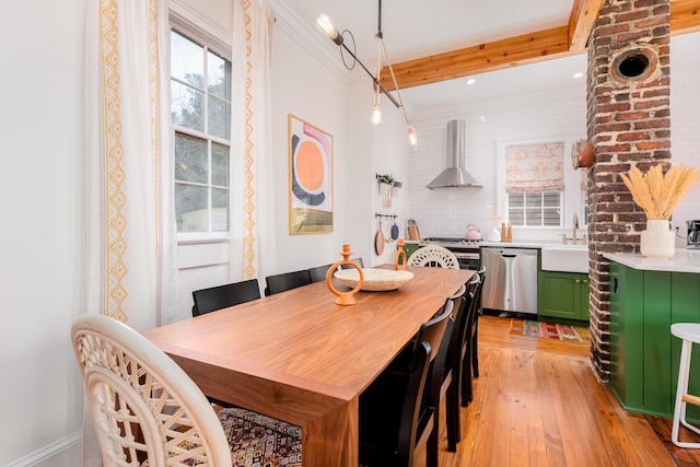 dining space featuring beam ceiling, light hardwood / wood-style floors, crown molding, and sink