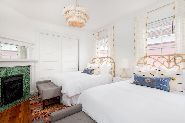 bedroom with an inviting chandelier, a tiled fireplace, ornamental molding, wood-type flooring, and a closet