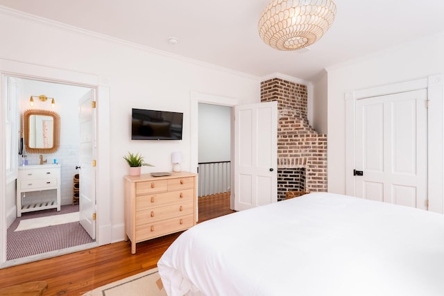 bedroom with hardwood / wood-style floors, crown molding, and a brick fireplace