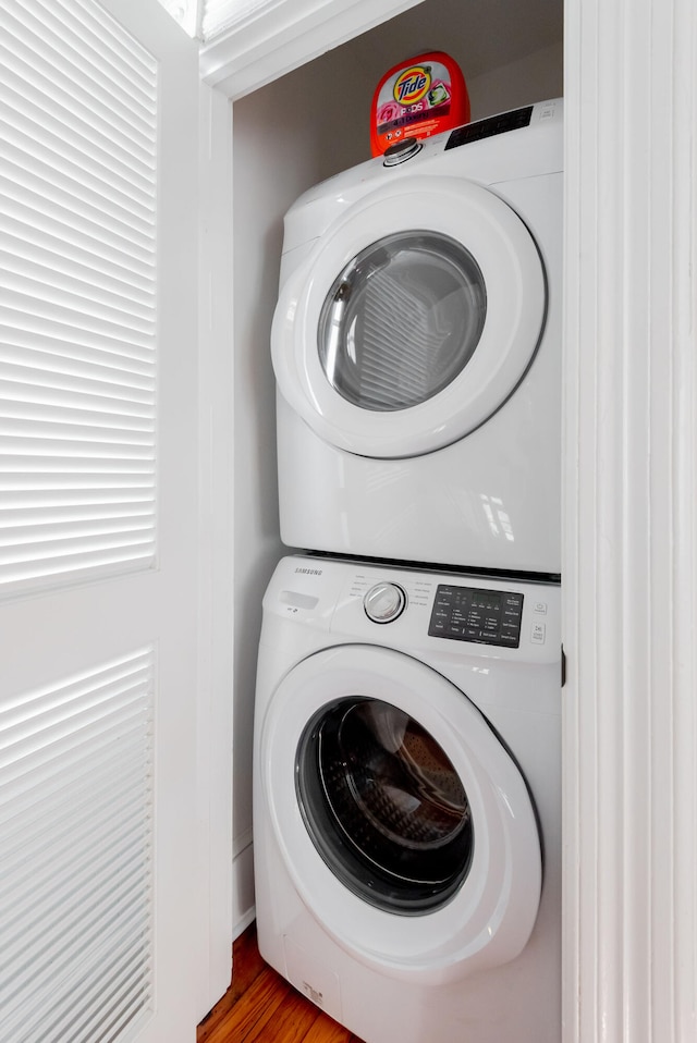 clothes washing area featuring hardwood / wood-style floors and stacked washing maching and dryer