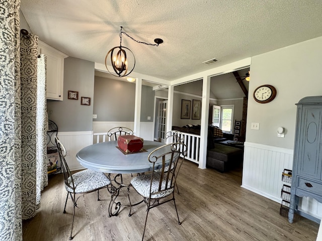 dining space featuring a textured ceiling, visible vents, wainscoting, wood finished floors, and ceiling fan with notable chandelier