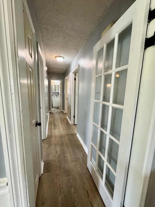 corridor with a textured ceiling, baseboards, and wood finished floors