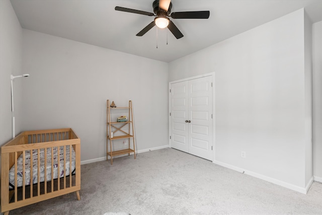carpeted bedroom with baseboards, a crib, and a ceiling fan