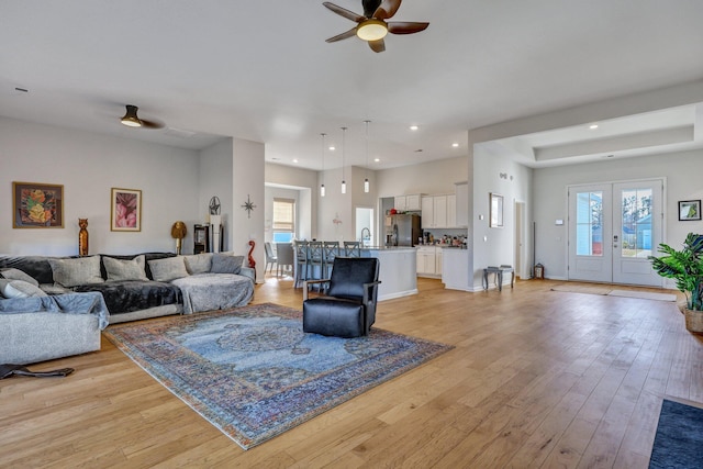 living room featuring light hardwood / wood-style flooring, french doors, sink, and ceiling fan