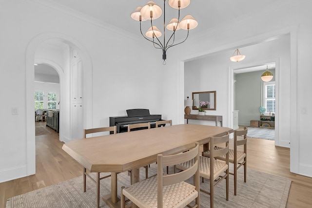 dining space featuring arched walkways, light wood-type flooring, baseboards, and ornamental molding