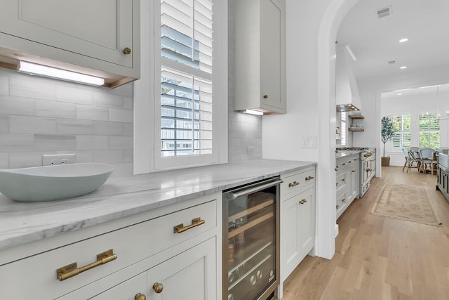 kitchen with beverage cooler, visible vents, light wood finished floors, decorative backsplash, and stainless steel stove