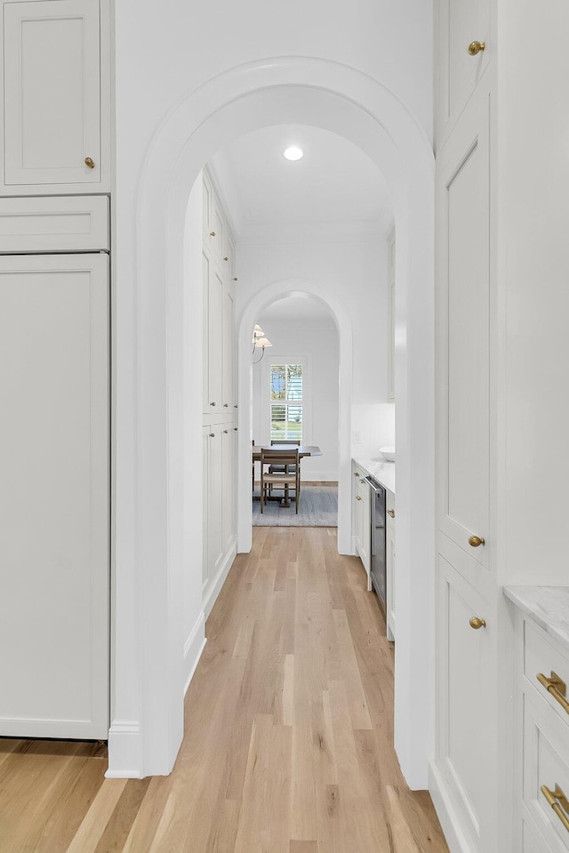 hallway featuring arched walkways and light wood finished floors