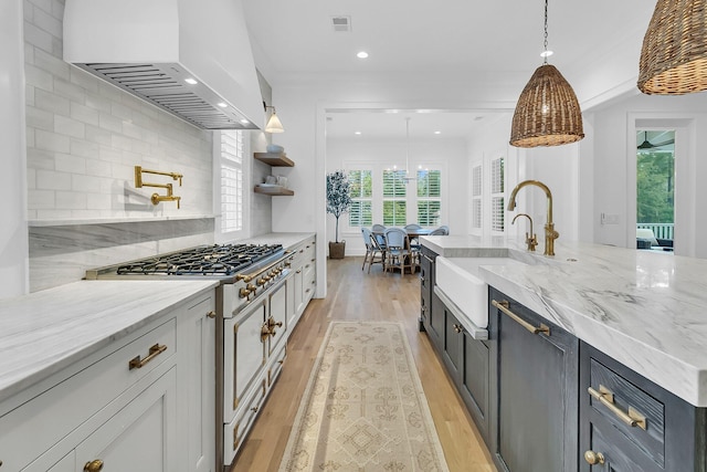 kitchen featuring light stone counters, custom exhaust hood, a sink, gas range oven, and light wood-style floors