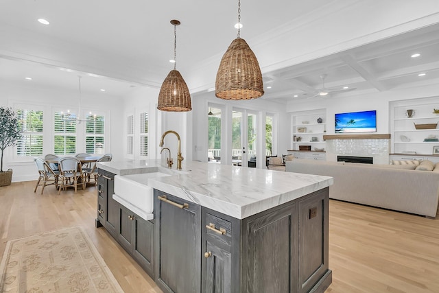 kitchen featuring a tiled fireplace, built in features, light wood-style floors, coffered ceiling, and a sink