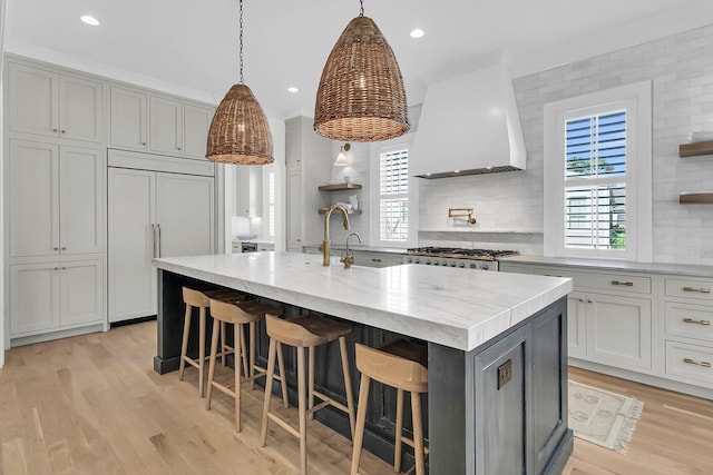 kitchen featuring open shelves, premium range hood, light wood-type flooring, paneled built in refrigerator, and a sink