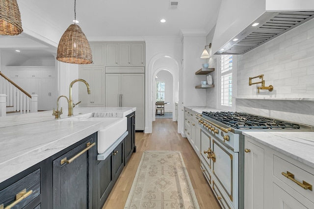 kitchen featuring arched walkways, a sink, light wood-style floors, gas range, and wall chimney range hood