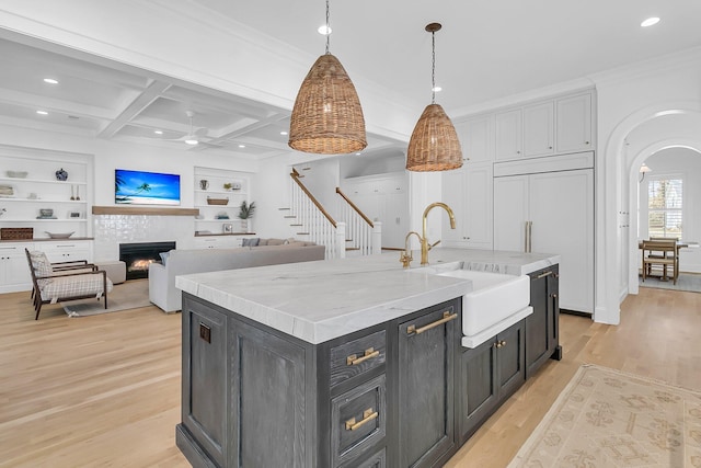 kitchen featuring a tiled fireplace, a sink, coffered ceiling, paneled built in fridge, and arched walkways