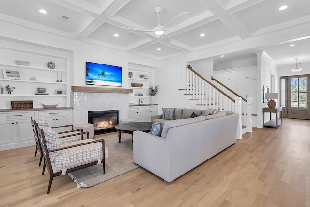 living area with built in features, stairway, beam ceiling, light wood-style floors, and coffered ceiling