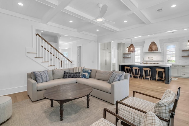 living area featuring beam ceiling, baseboards, light wood-type flooring, and coffered ceiling