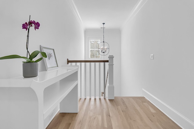 hallway featuring baseboards, a chandelier, ornamental molding, an upstairs landing, and wood finished floors