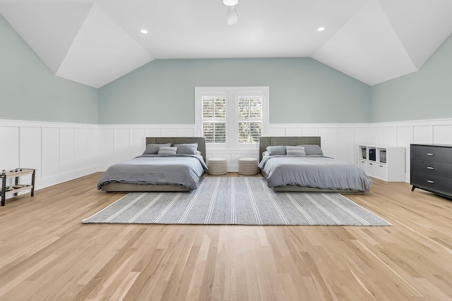 bedroom with wainscoting, light wood-style floors, and vaulted ceiling