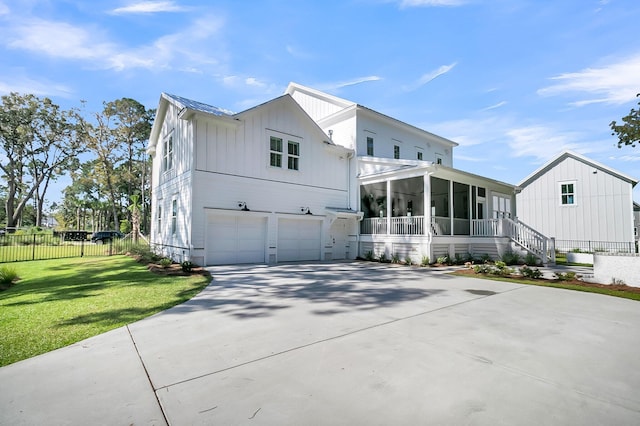 modern farmhouse featuring board and batten siding, concrete driveway, a front yard, a sunroom, and a garage